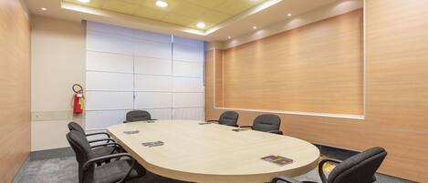 A conference room with a long table, six chairs, and a fire extinguisher on the wall.