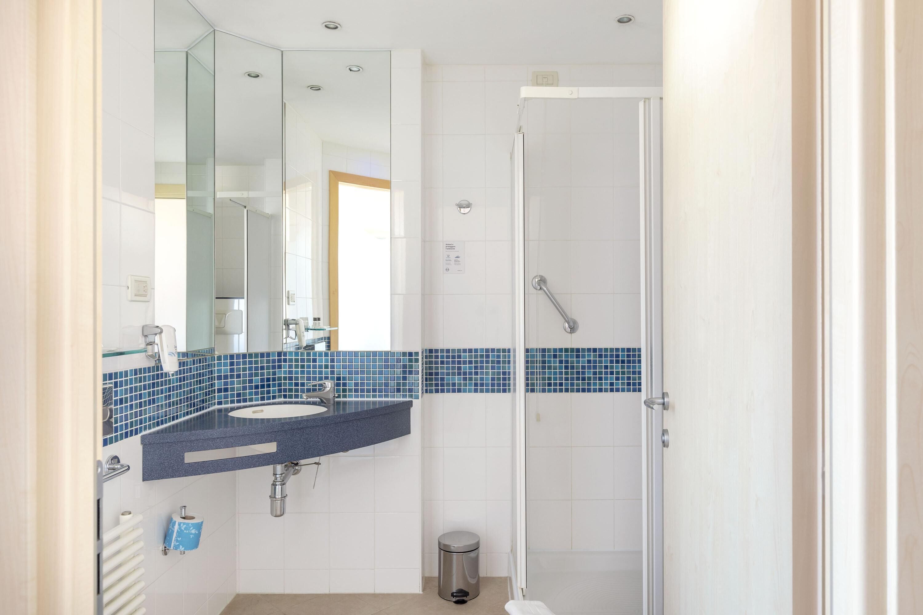 A modern bathroom with a blue-tiled shower area, a white sink, and a glass shower enclosure.