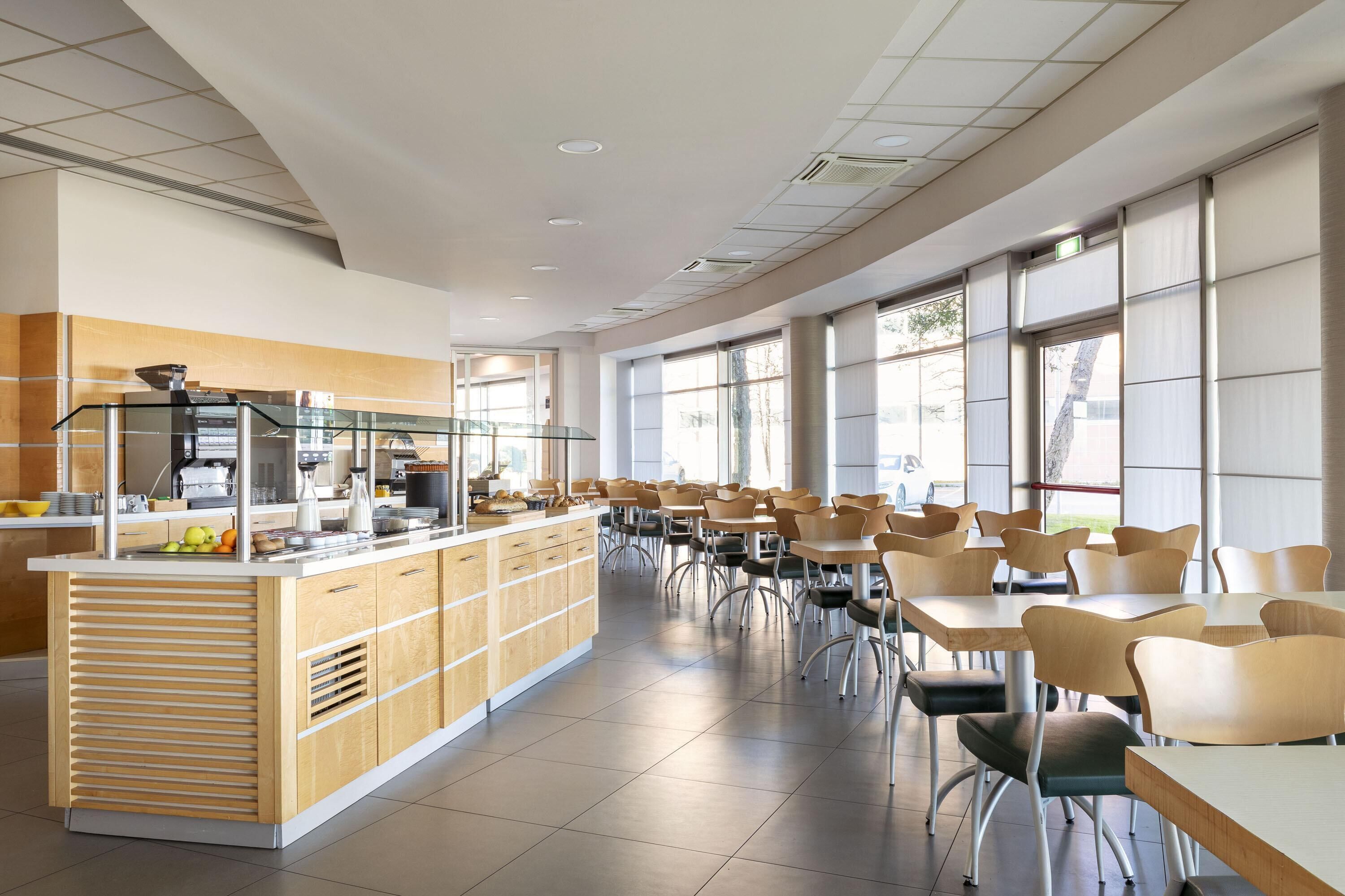 Una amplia cafetería con una barra larga, varias mesas y sillas.