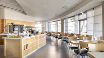 Una amplia cafetería con una barra larga, varias mesas y sillas.