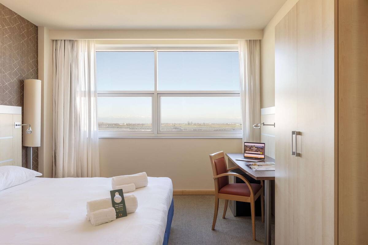 Een hotelkamer met een bed, een bureau en uitzicht op de stads skyline.