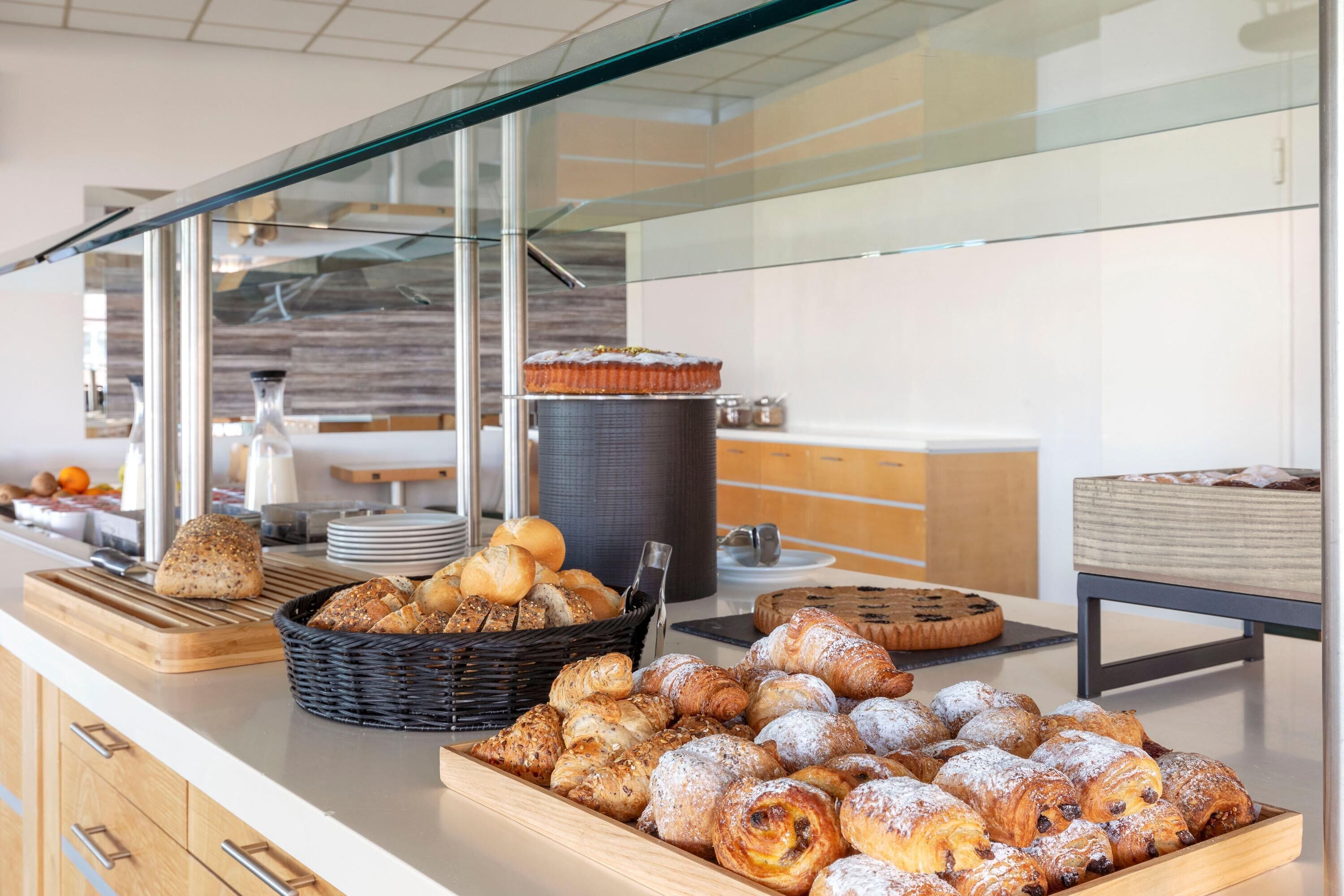 A buffet counter with various baked goods, including bread, pastries, and a cake.