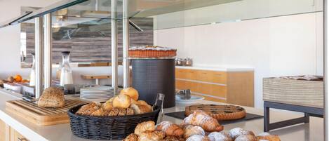 A buffet counter with various baked goods, including bread, pastries, and a cake.