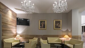 A lobby with a wooden wall, two paintings, a TV, and a chandelier. - Hotel Falco D'Oro by Falco D'Oro Hotels (Vergato)