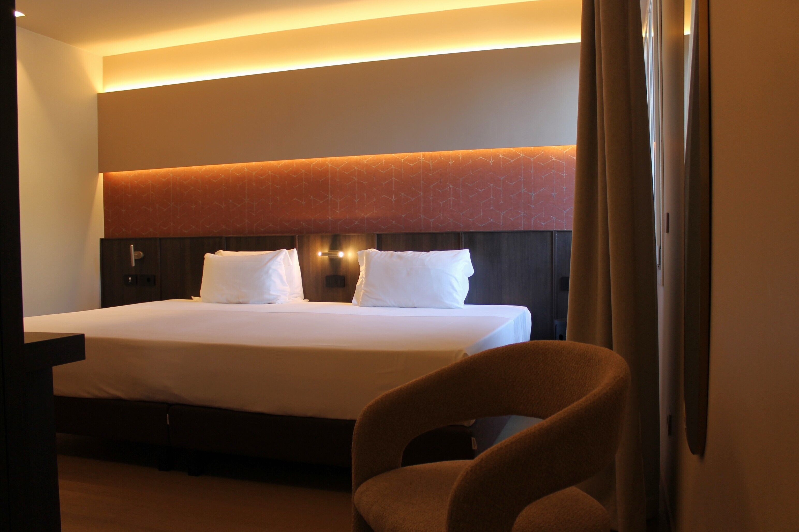 Una habitación de hotel con una cama grande, un cabecero de diseño geométrico y una silla.