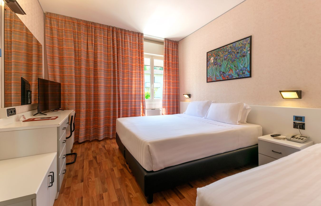 Una camera d'albergo con un letto, un comodino, una lampada e un quadro appeso al muro.