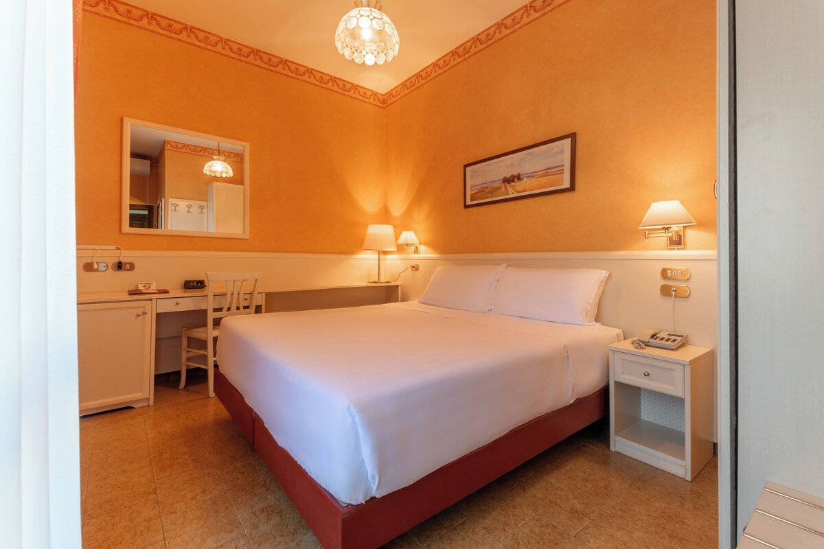 Ein Hotelzimmer mit einem Einzelbett, Nachttisch, Lampe und Schreibtisch mit Stuhl.