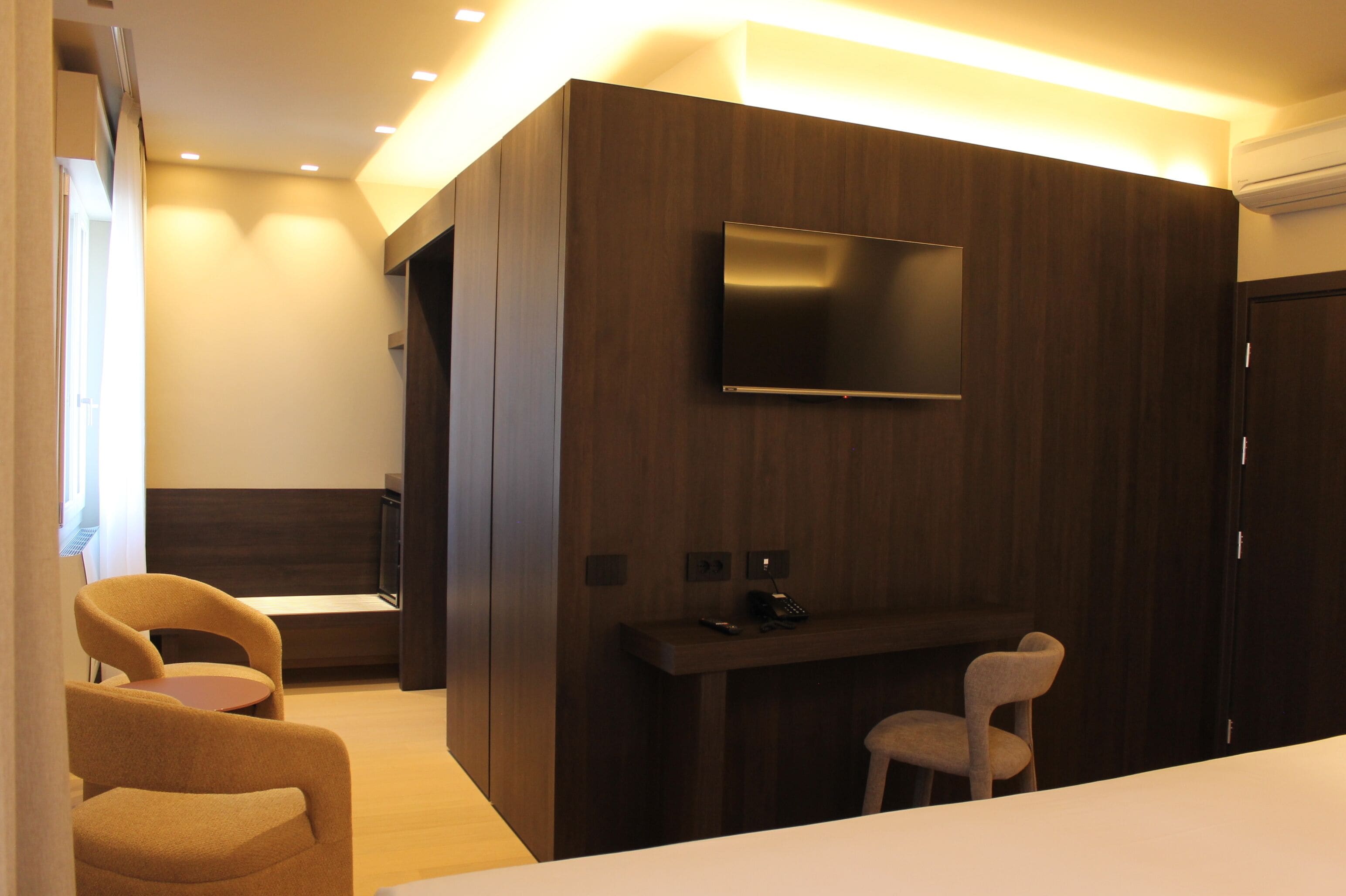 Habitación moderna con televisor de pantalla plana montado en una pared de paneles de madera oscura, un escritorio pequeño con teléfono y dos sillas.