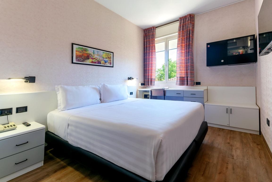 A hotel room with a bed, bedside table, lamp, and a window with curtains.