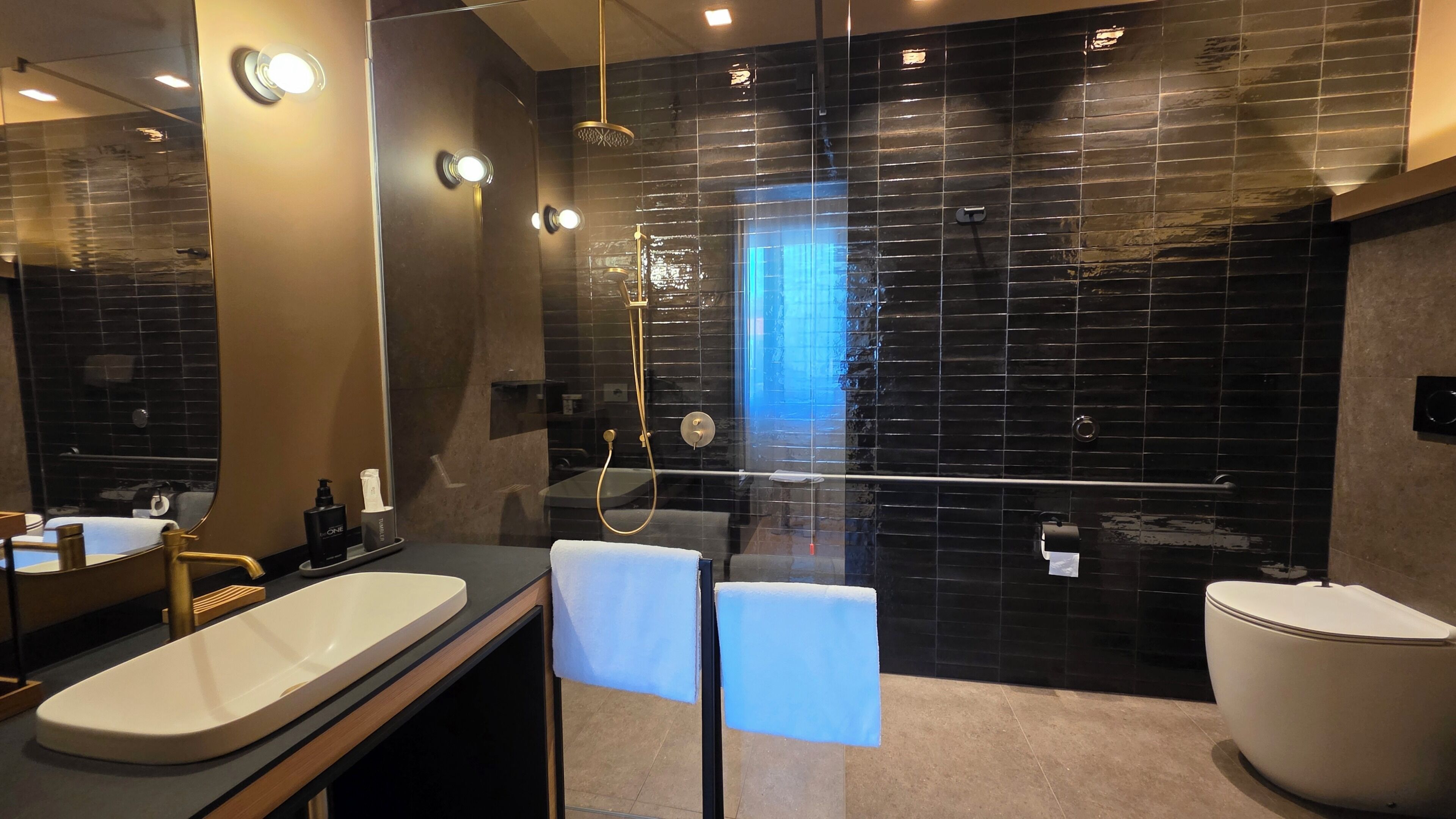A modern bathroom with a large mirror, dual sinks, a shower with a glass door, and a toilet.
