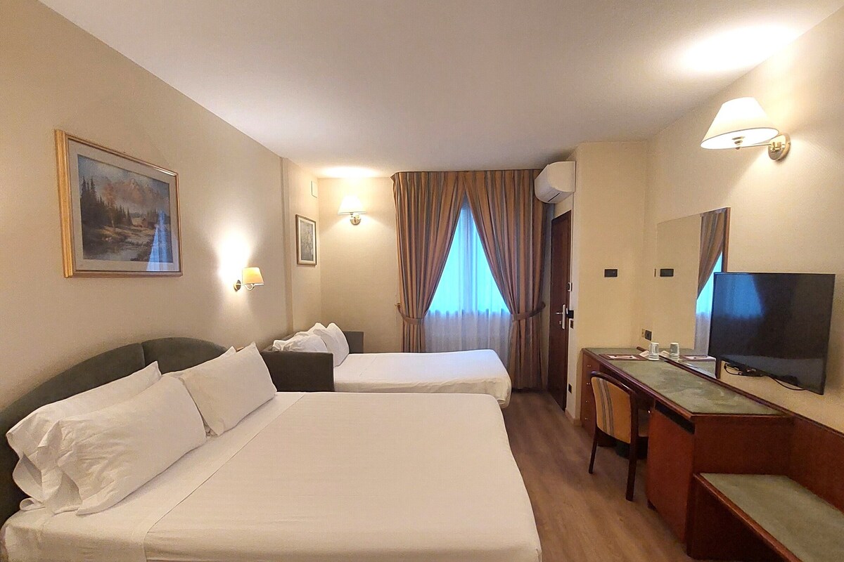 A hotel room with two beds, a desk, a television, and a window with curtains.