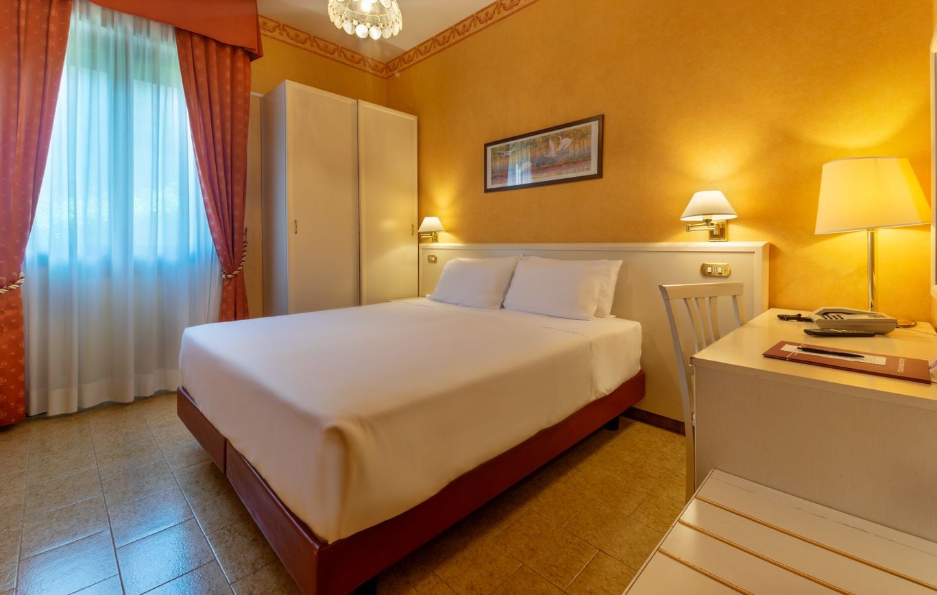 Una habitación de hotel con cama, mesita de noche, lámpara y un cuadro en la pared.