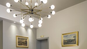 A lobby with wicker chairs, a chandelier, and two framed paintings on the walls. - Hotel Falco D'Oro by Falco D'Oro Hotels (Vergato)