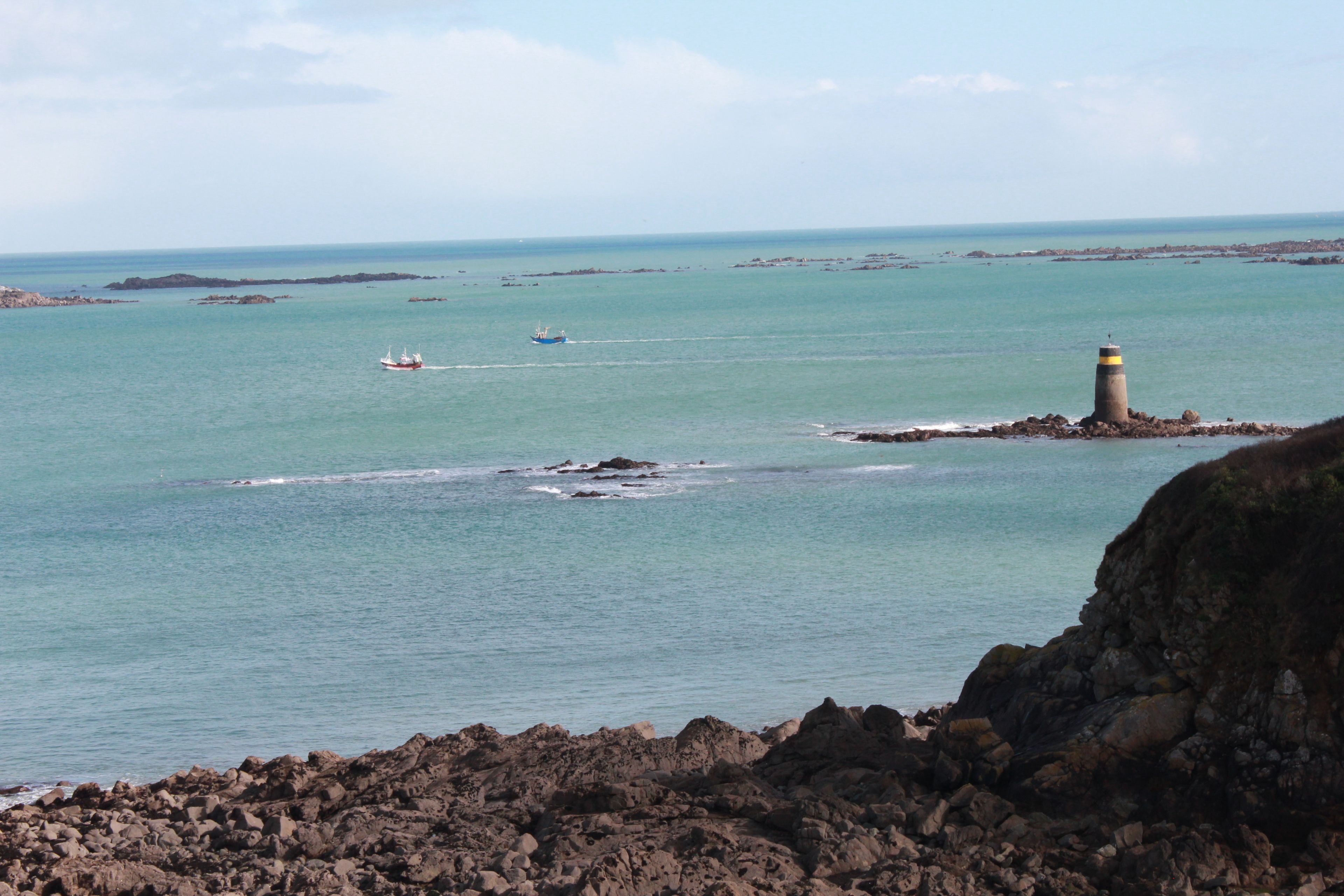 A coastal scene with a rocky shoreline, calm sea, and a lighthouse.