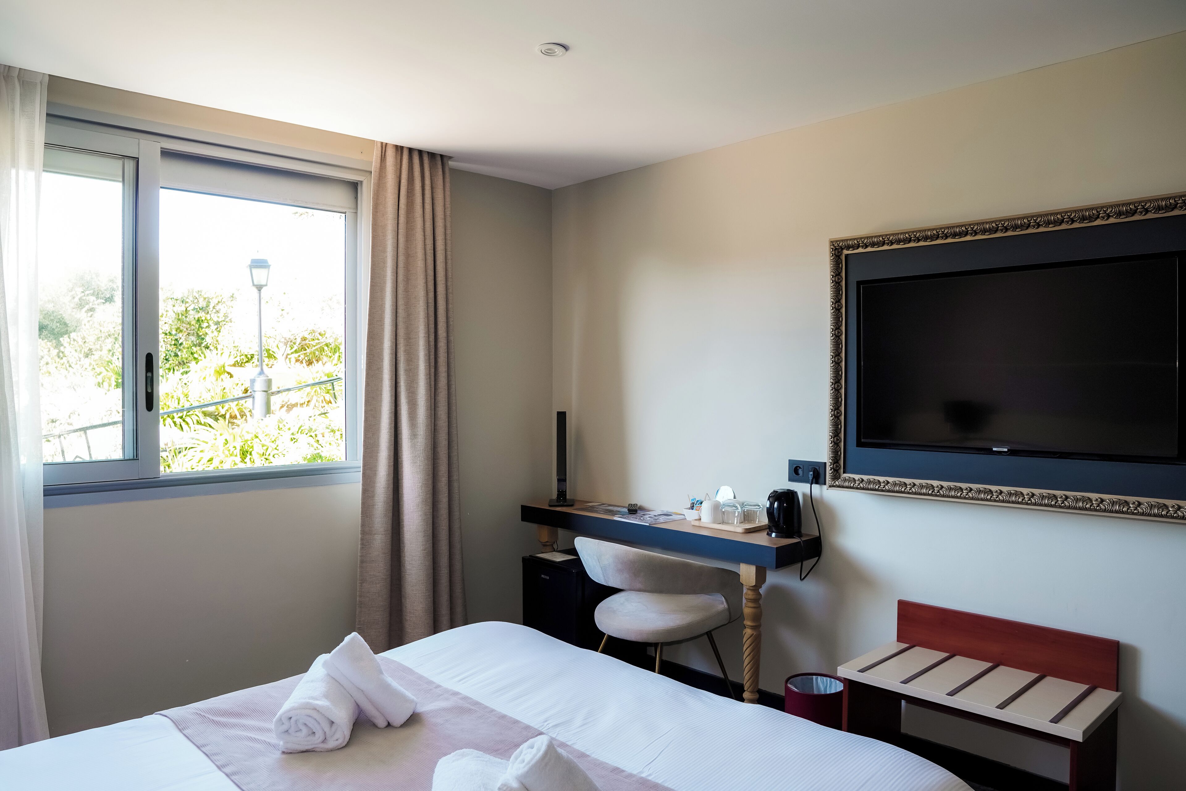 Una habitación de hotel con cama, escritorio, silla, televisor y ventana con cortinas.