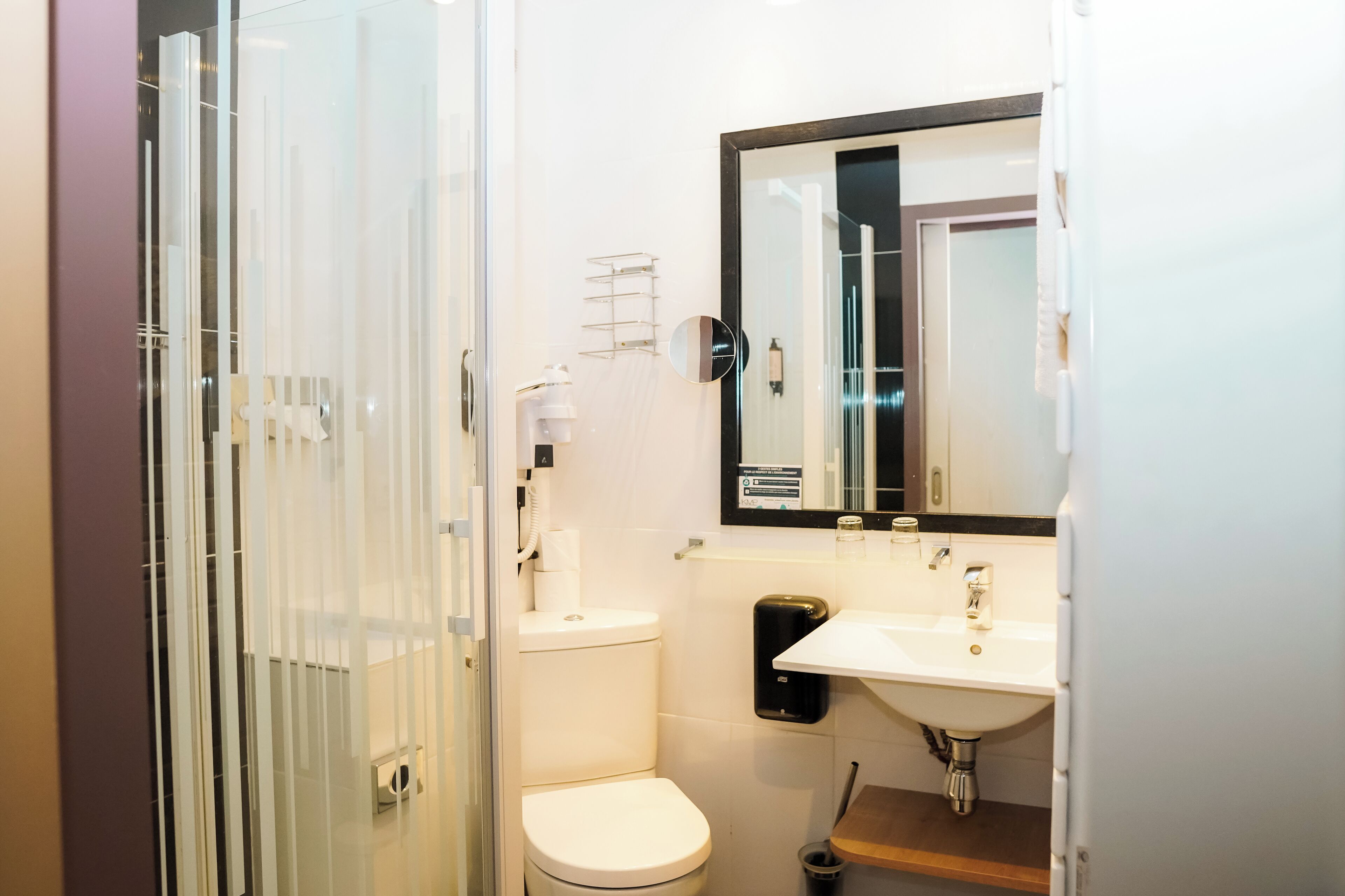 Une salle de bain moderne avec une douche à parois de verre, des toilettes, un lavabo avec un miroir et un distributeur de savon.