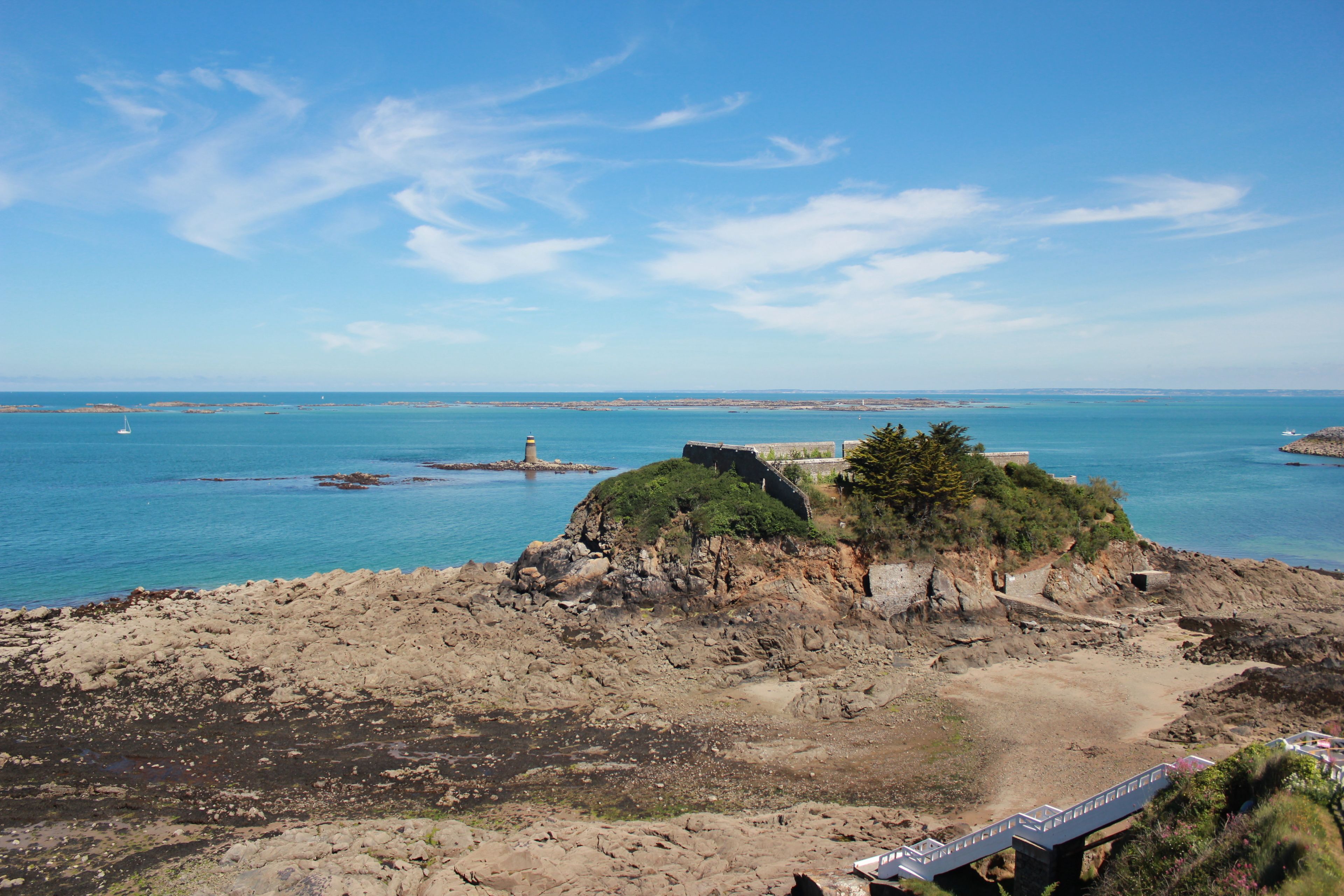 A coastal landscape with rocky terrain, a lighthouse, and a fortified structure.