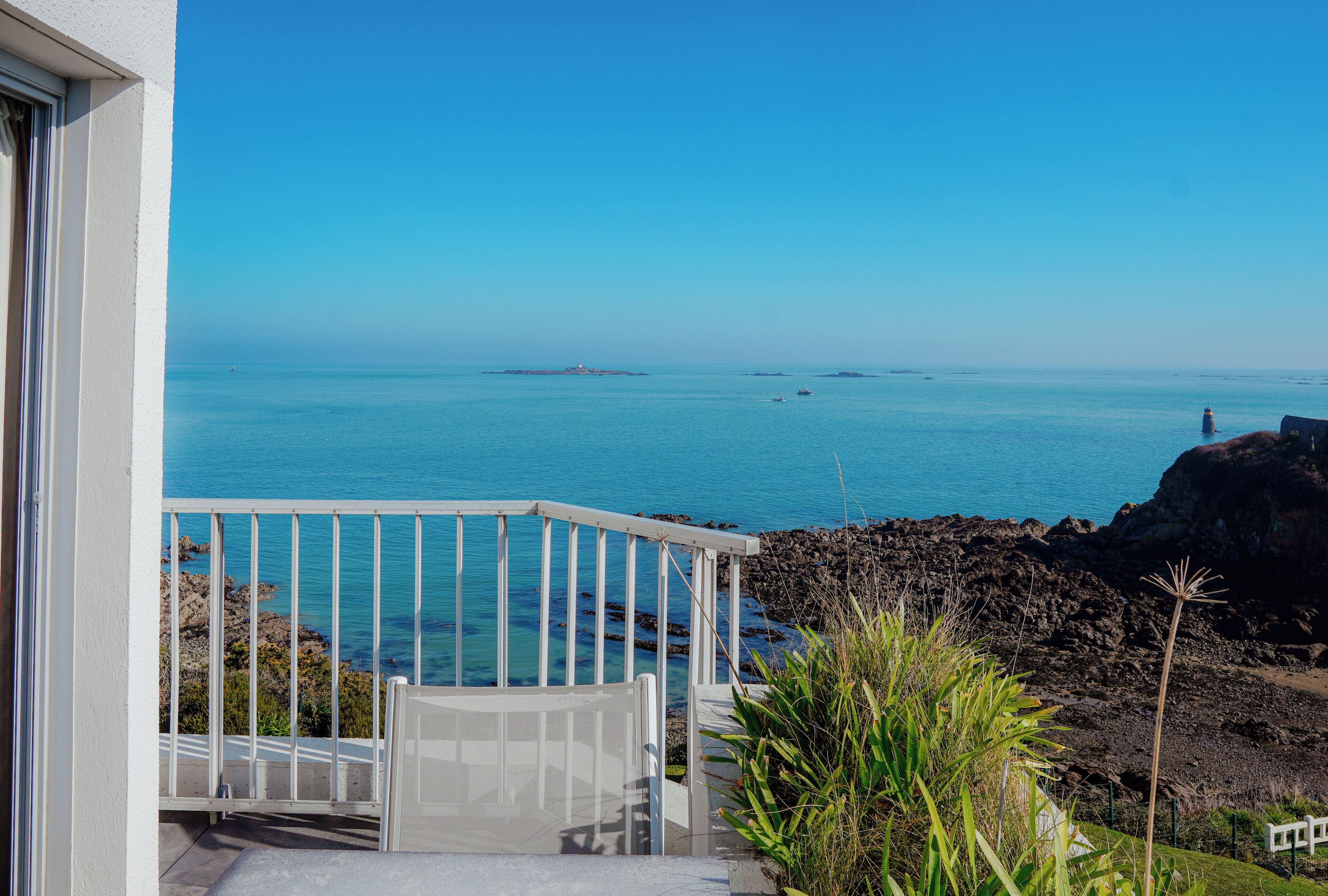 A balcony with a view of the sea, rocky terrain, and a lighthouse in the distance.
