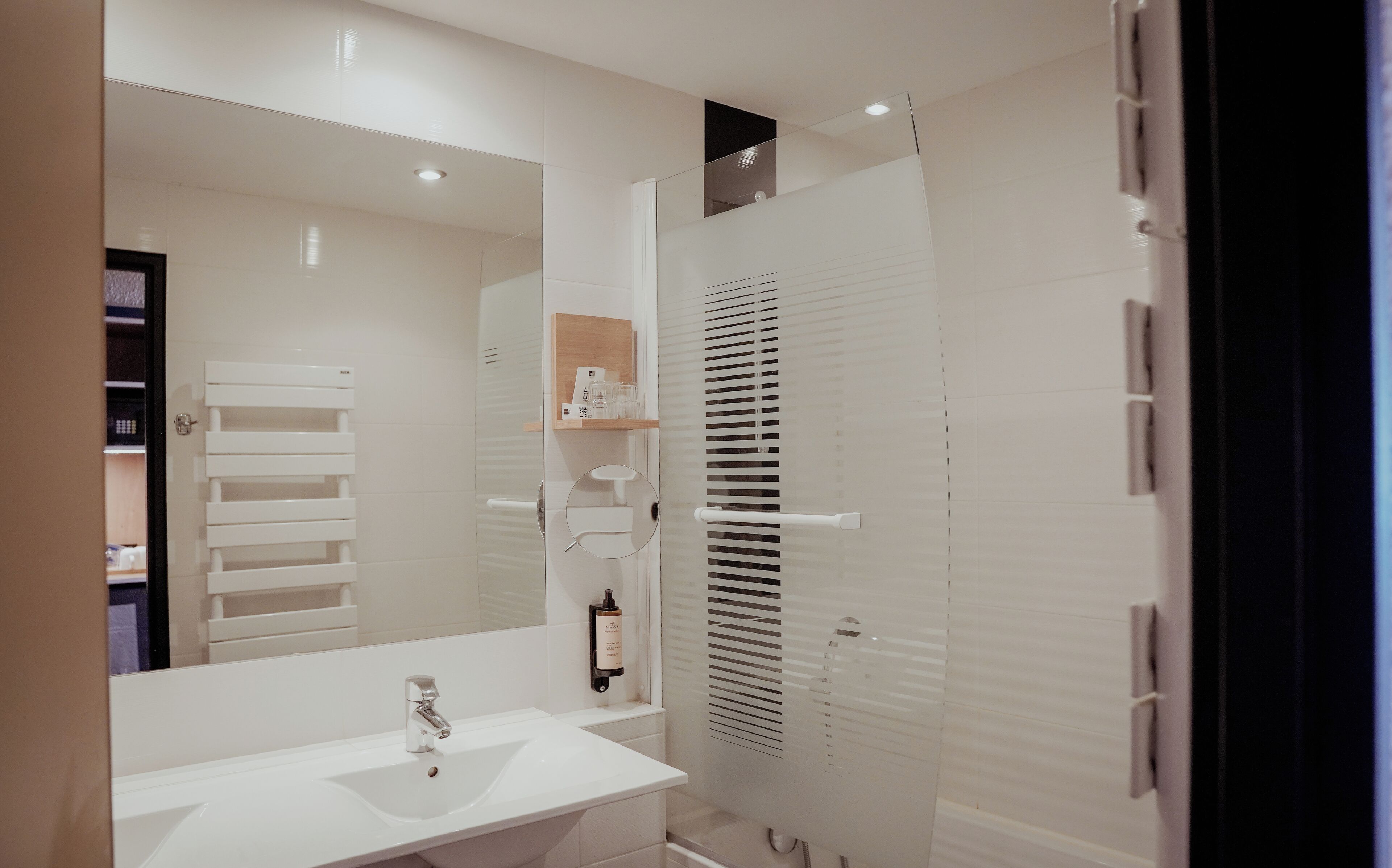 Un baño moderno con lavamanos blanco, espejo y cabina de ducha con puerta de vidrio.