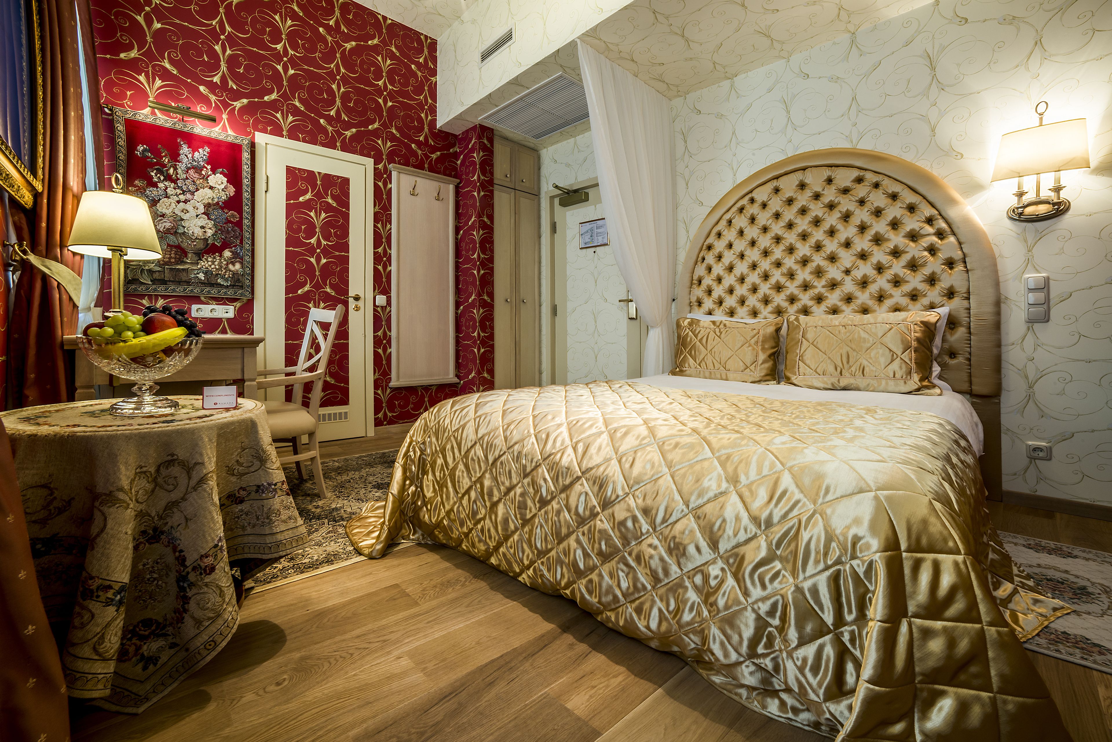 Un dormitorio con una cama grande, una mesita de noche con lámpara, un frutero y una puerta que da a otra habitación.