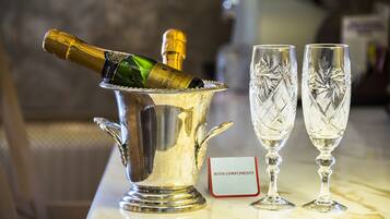 A champagne bottle in a silver ice bucket with two crystal glasses beside it, and a sign that reads "WITH COMPLIMENTS".