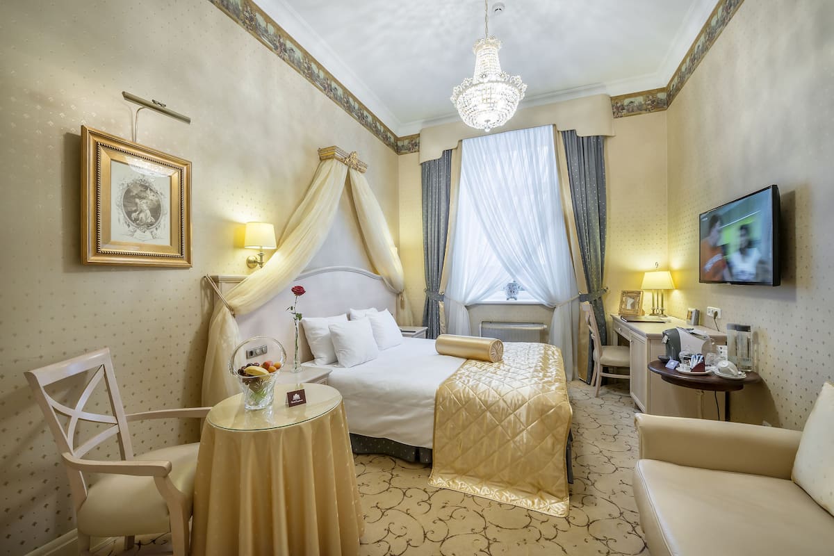 Habitación de hotel con cama, escritorio, silla, televisor y candelabro.