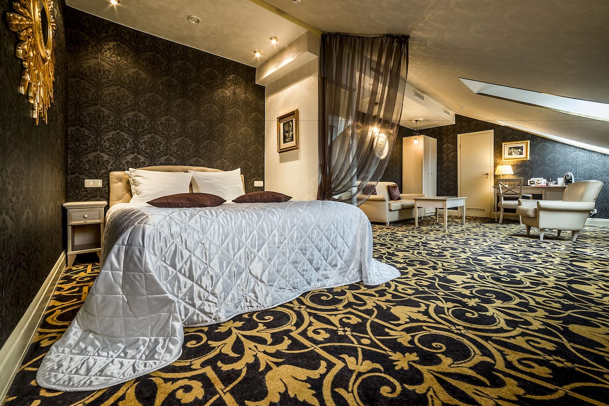 Habitación de hotel con una cama grande, un escritorio, una silla y una alfombra estampada.