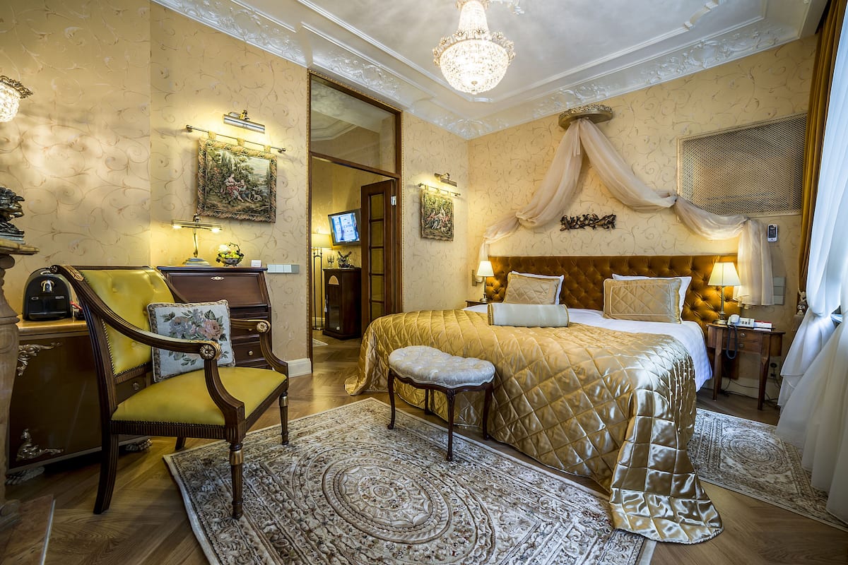 Un dormitorio lujoso con una cama grande, un sillón, una mesita de noche de madera y un candelabro.