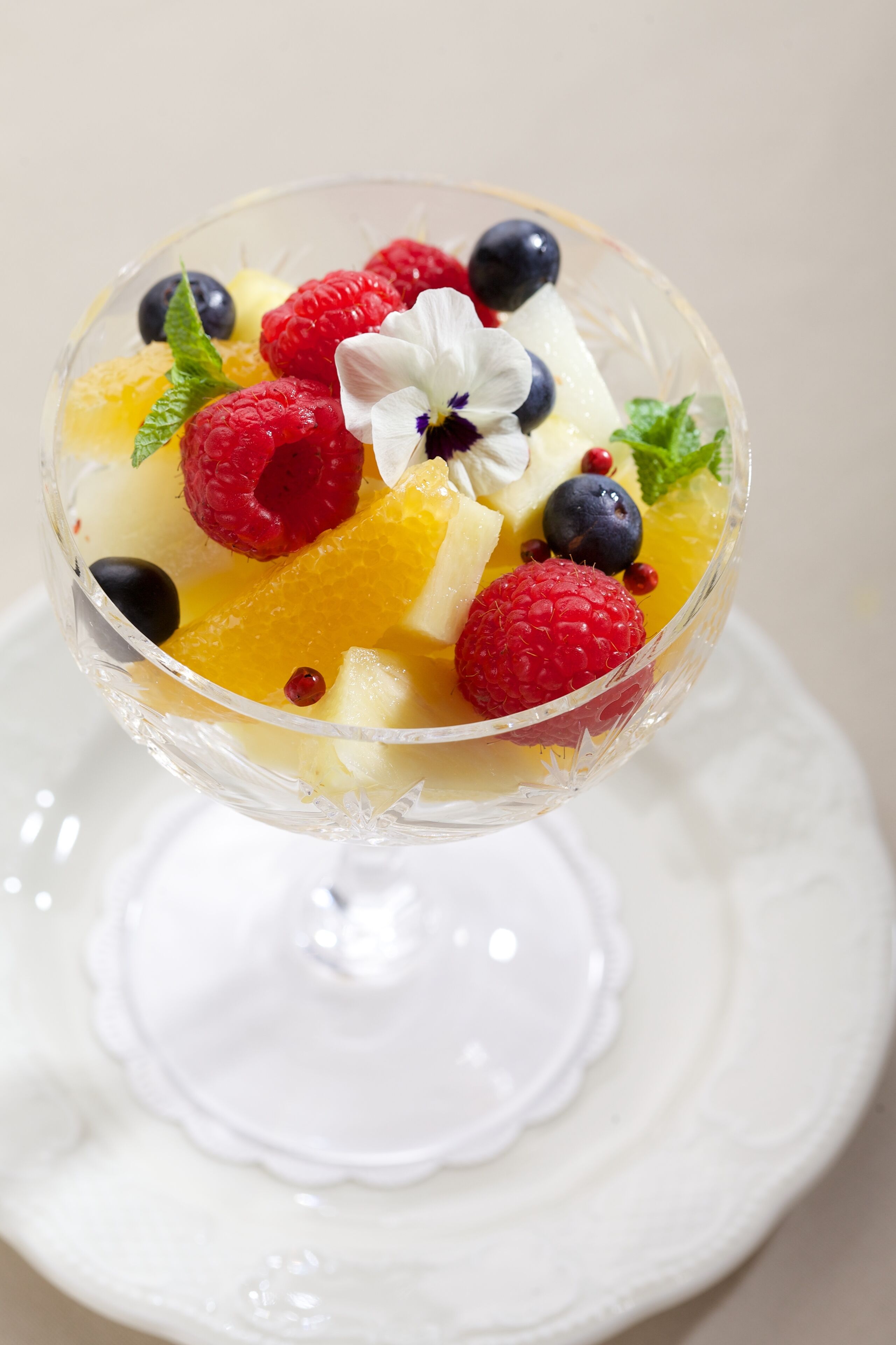 A dessert in a glass bowl with various fruits and a flower on top.