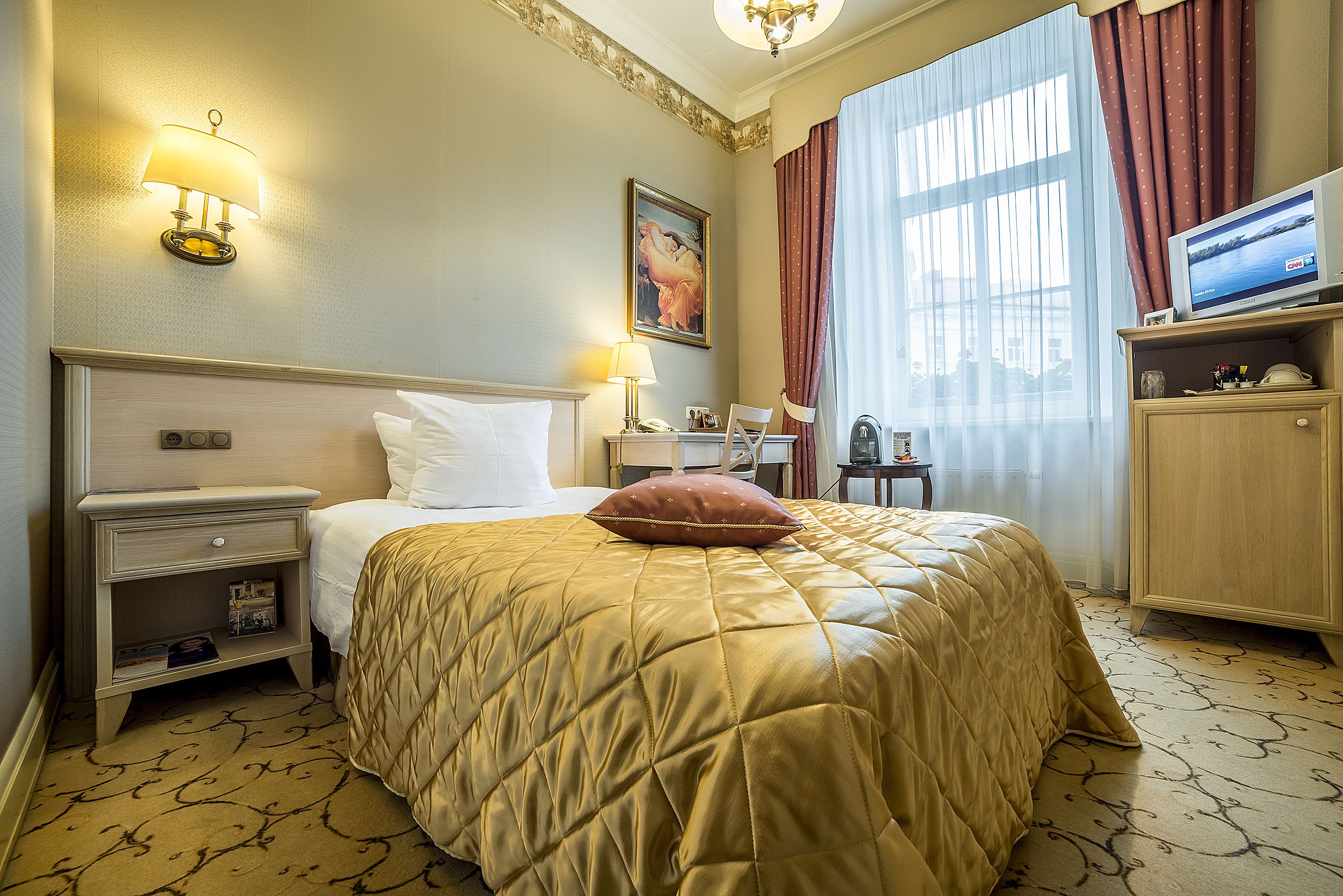 Una habitación de hotel con cama, mesita de noche, televisor y ventana con cortinas.