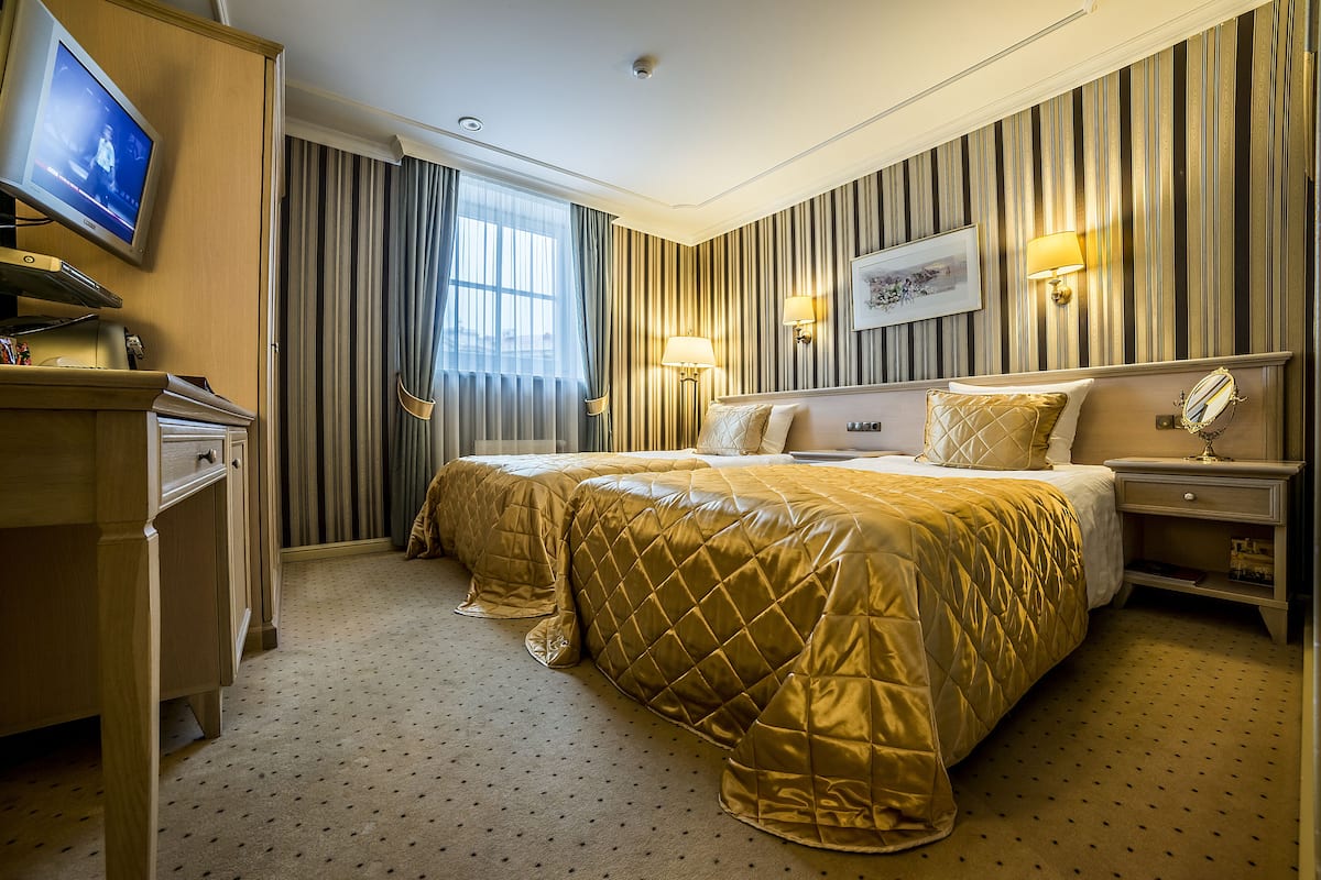 Una habitación de hotel con una cama grande, un escritorio con televisor y un ventanal con cortinas.