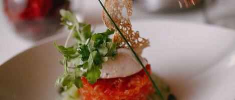 Un plato blanco con un plato gourmet, adornado con vegetales y un detalle decorativo.