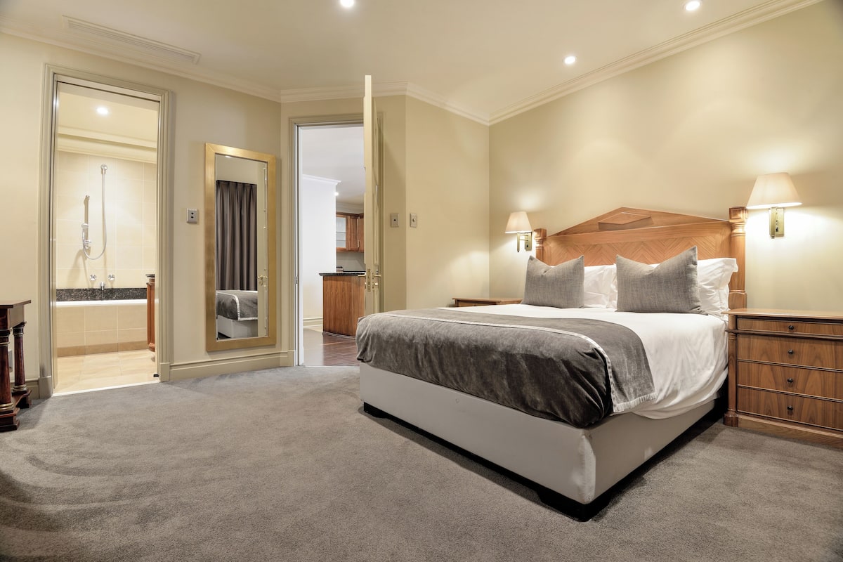Een slaapkamer met een groot bed, nachtlampjes, een houten hoofdbord en een vloerbedekking.