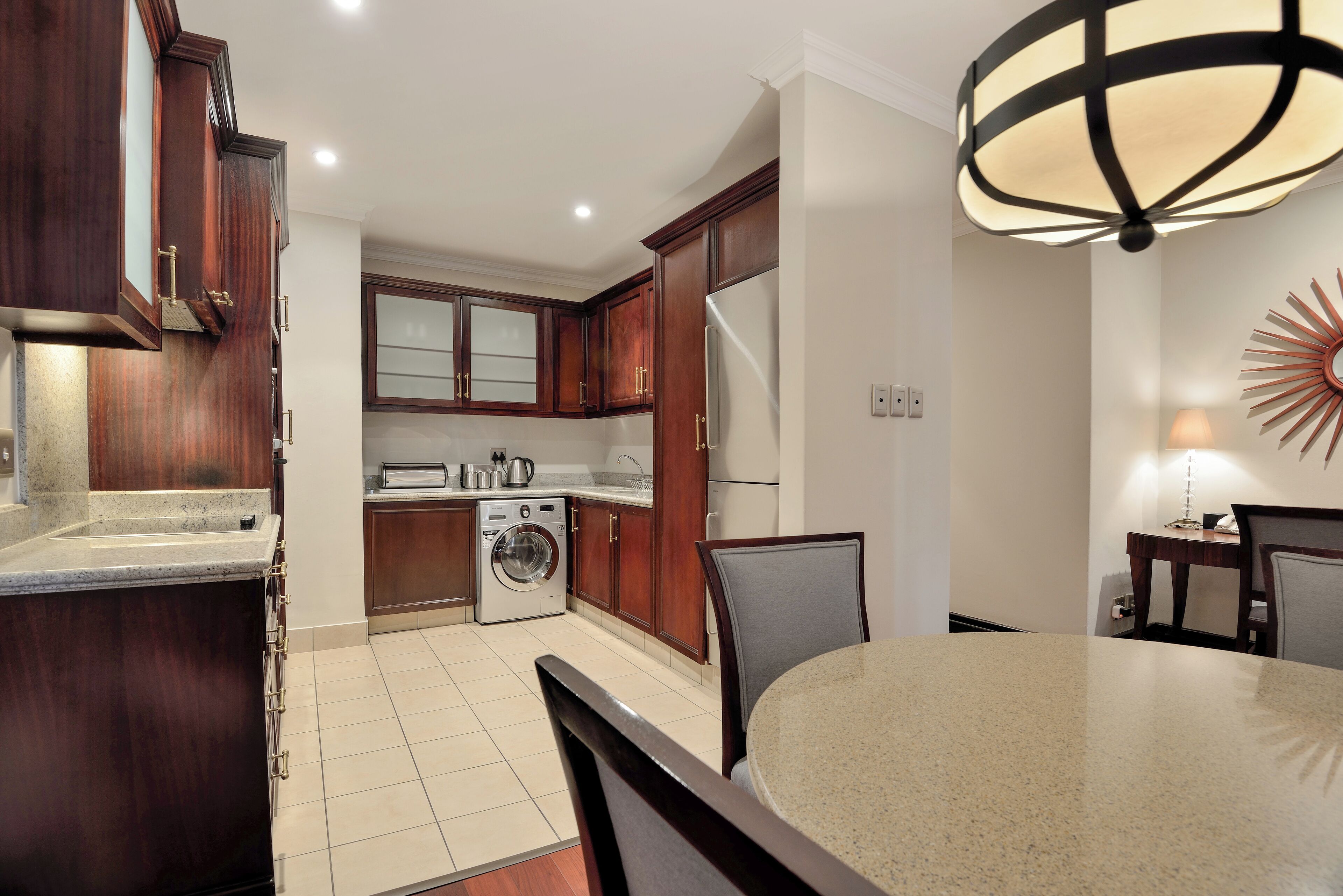 A modern kitchen with wooden cabinets, a built-in washing machine, and a dining area with a round table and chairs.
