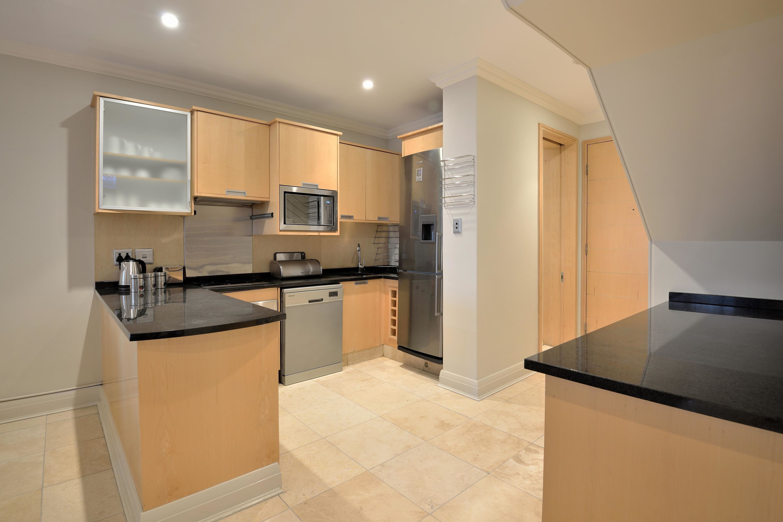 A modern kitchen with wooden cabinets, a stainless steel refrigerator, a microwave, and a dishwasher.