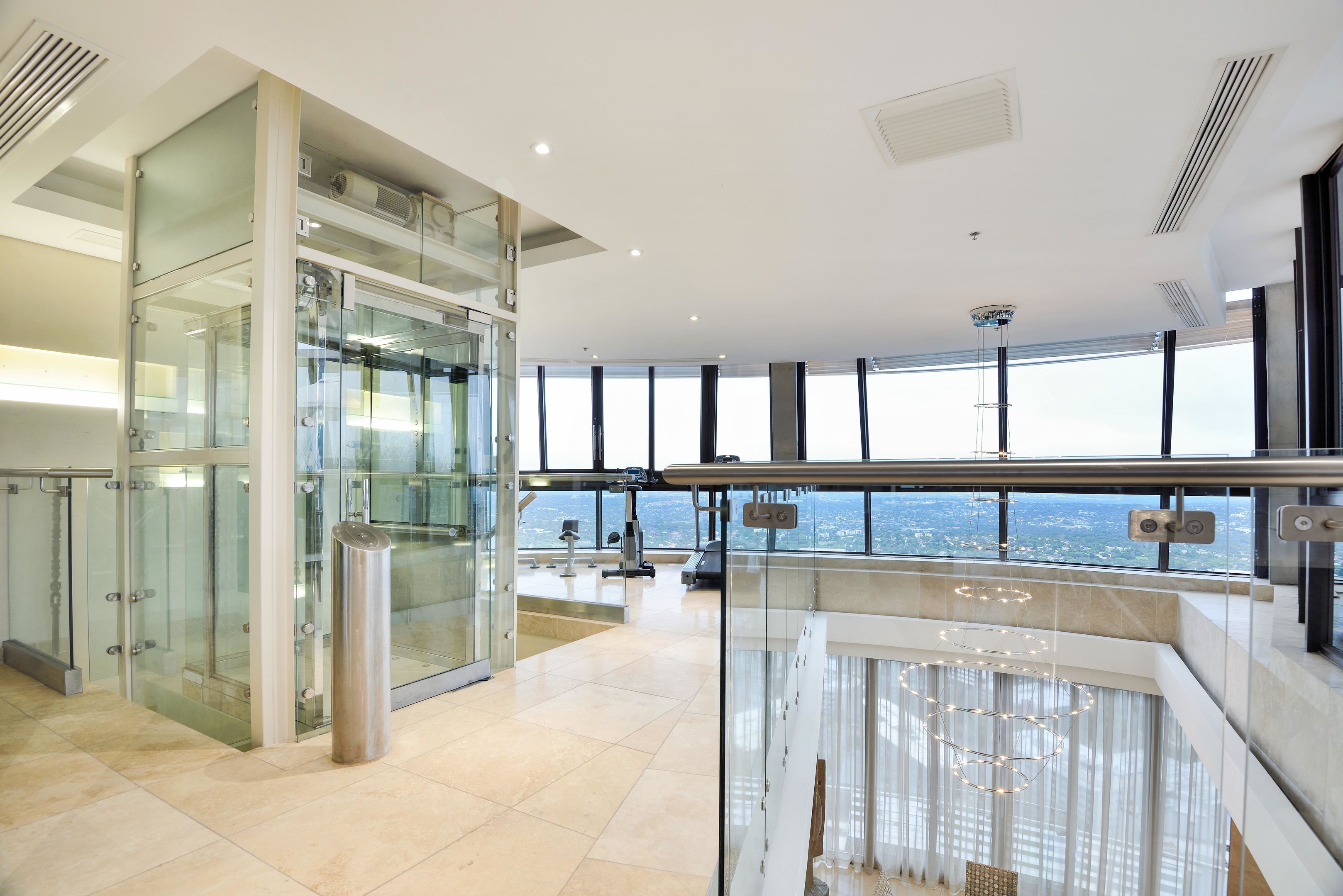 Un hall d’hôtel moderne doté d’un ascenseur en verre, offrant une vue sur la ville, et d’un espace spacieux agrémenté d’une rambarde.