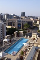 Μια πισίνα στην ταράτσα, με ξαπλώστρες και ομπρέλες, που περιβάλλεται από κτίρια.