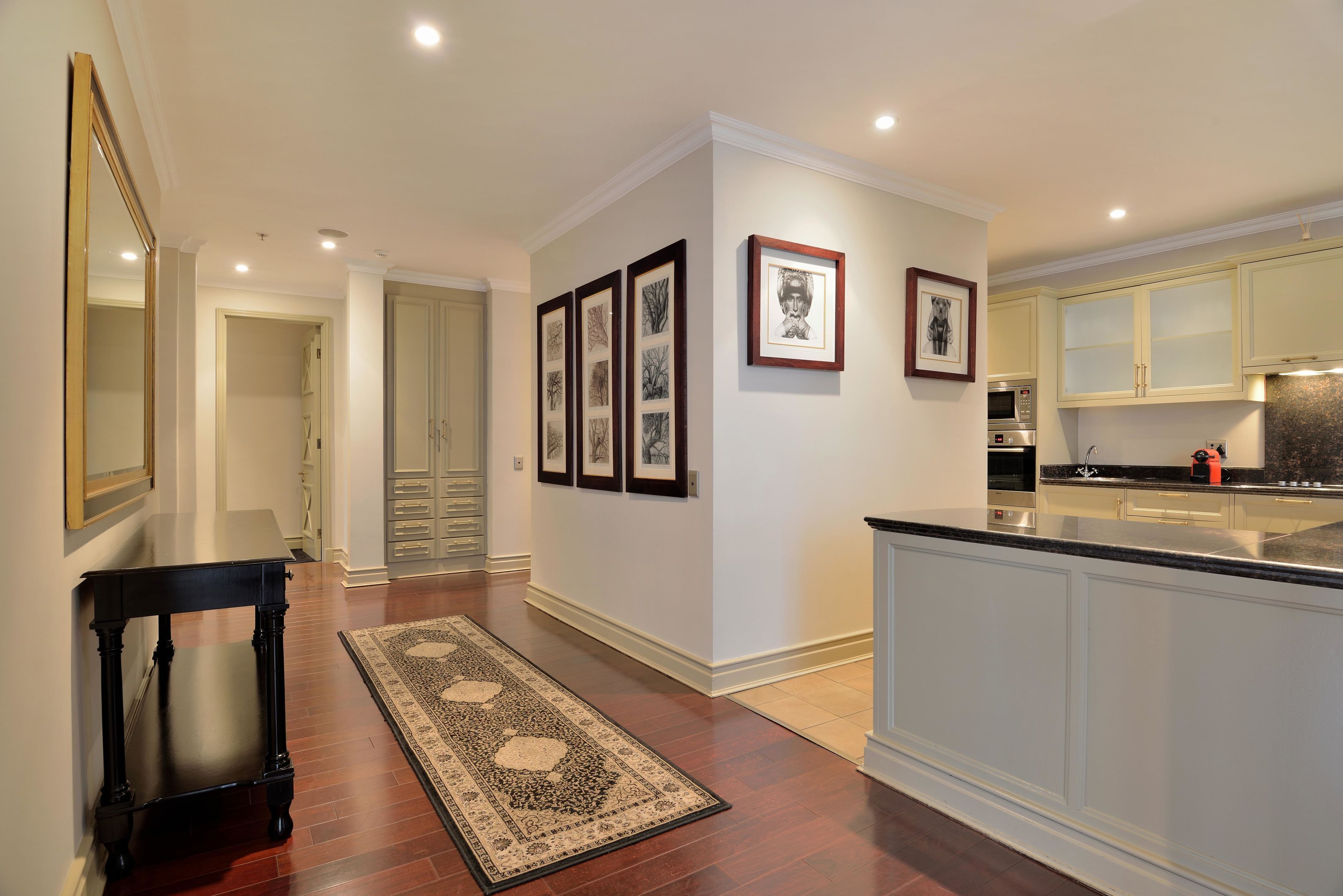 A hallway with a wooden table, a patterned rug, and framed pictures on the wall.