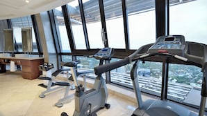 Een fitnessruimte met trainingsapparatuur en grote ramen met uitzicht op de stad.