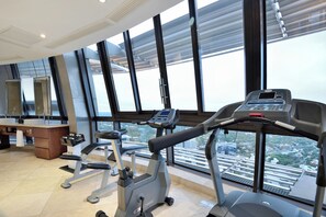 Ein Fitnessstudio mit Trainingsgeräten und großen Fenstern, die einen Blick auf die Stadt ermöglichen.
