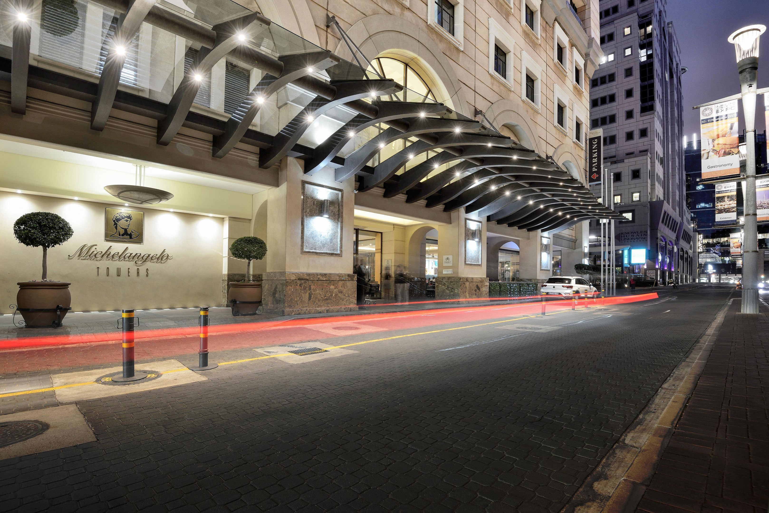 A hotel facade with a modern design, featuring a prominent arch structure and a sign that reads "Michelangelo Towers."