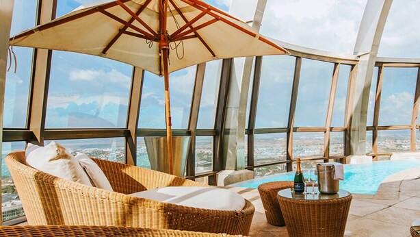 Hotelkamer in een wolkenkrabber met een groot raam, een privézwembad, rieten meubels en een tafel met drankjes.