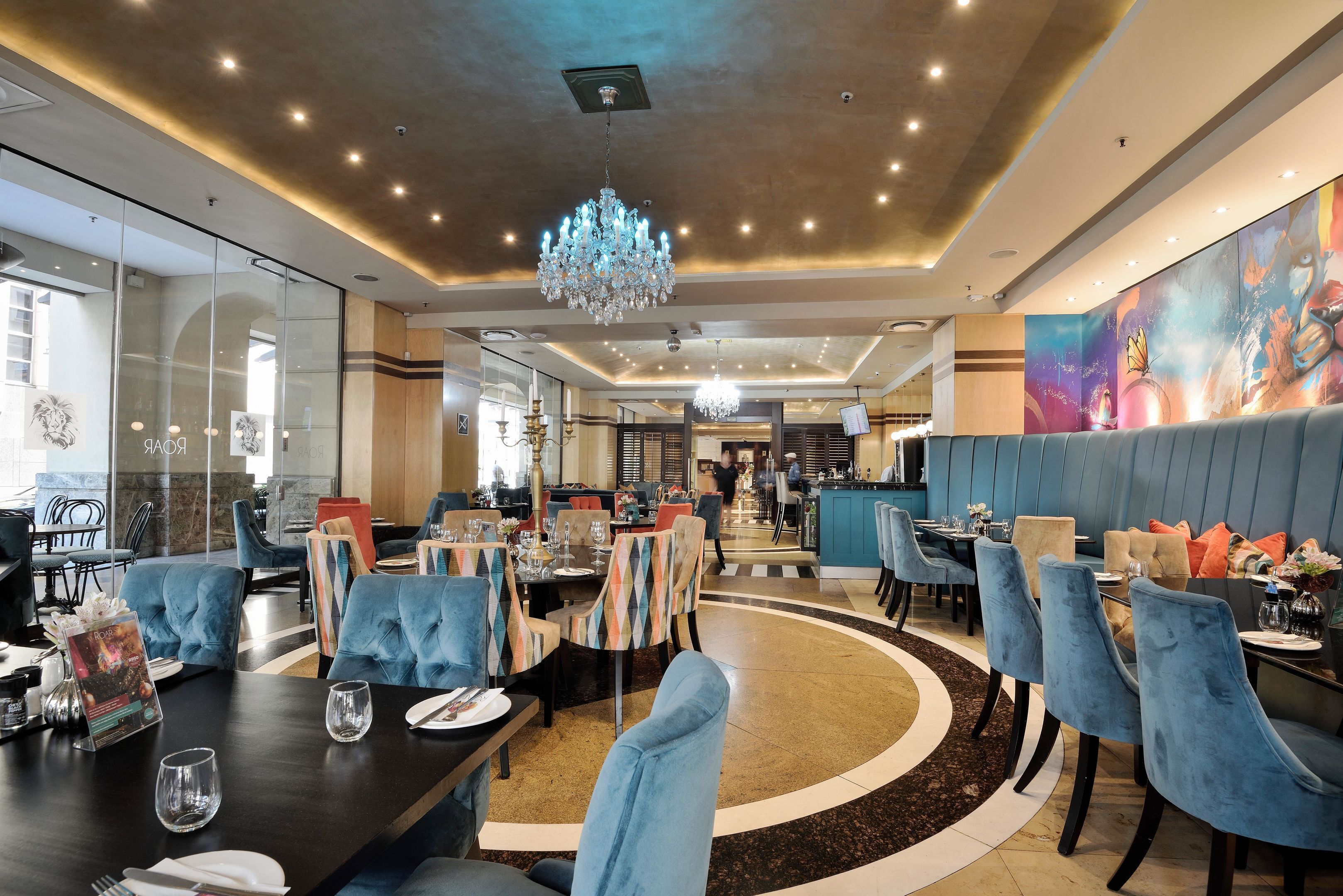 Een restaurant met ronde tafels, blauwe gestoffeerde stoelen en een kroonluchter.