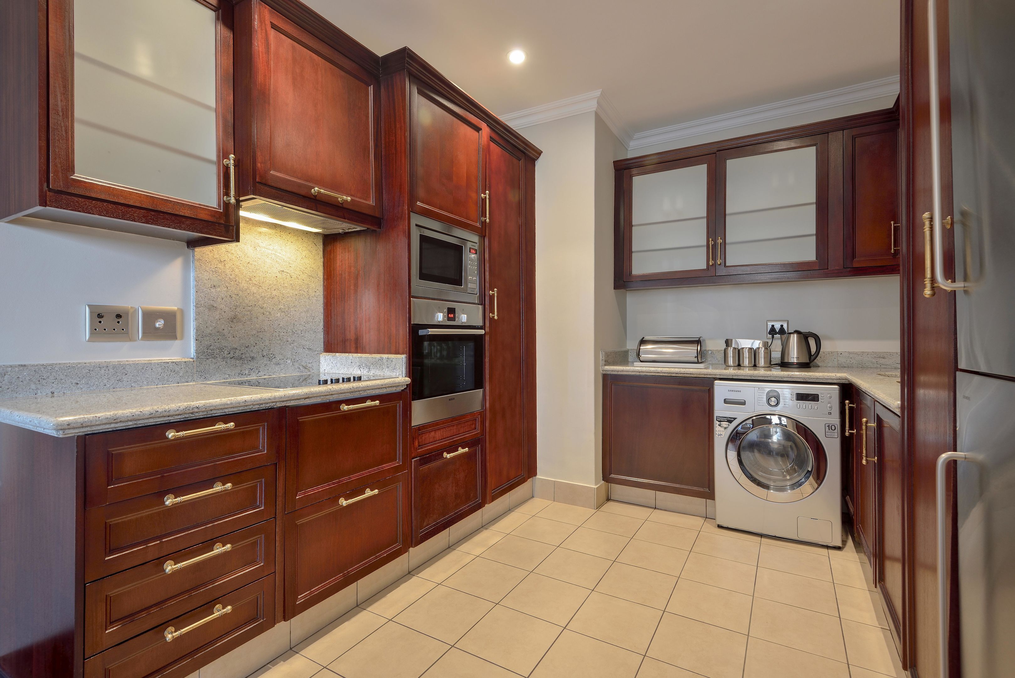 Una cucina compatta con mobili in legno, un forno a microonde integrato, forno e lavatrice.