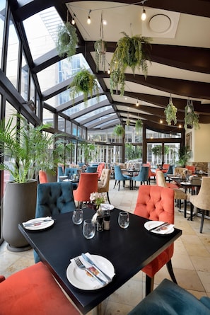 Un restaurant moderne doté de grandes fenêtres, de plantes suspendues et offrant différents types de sièges.