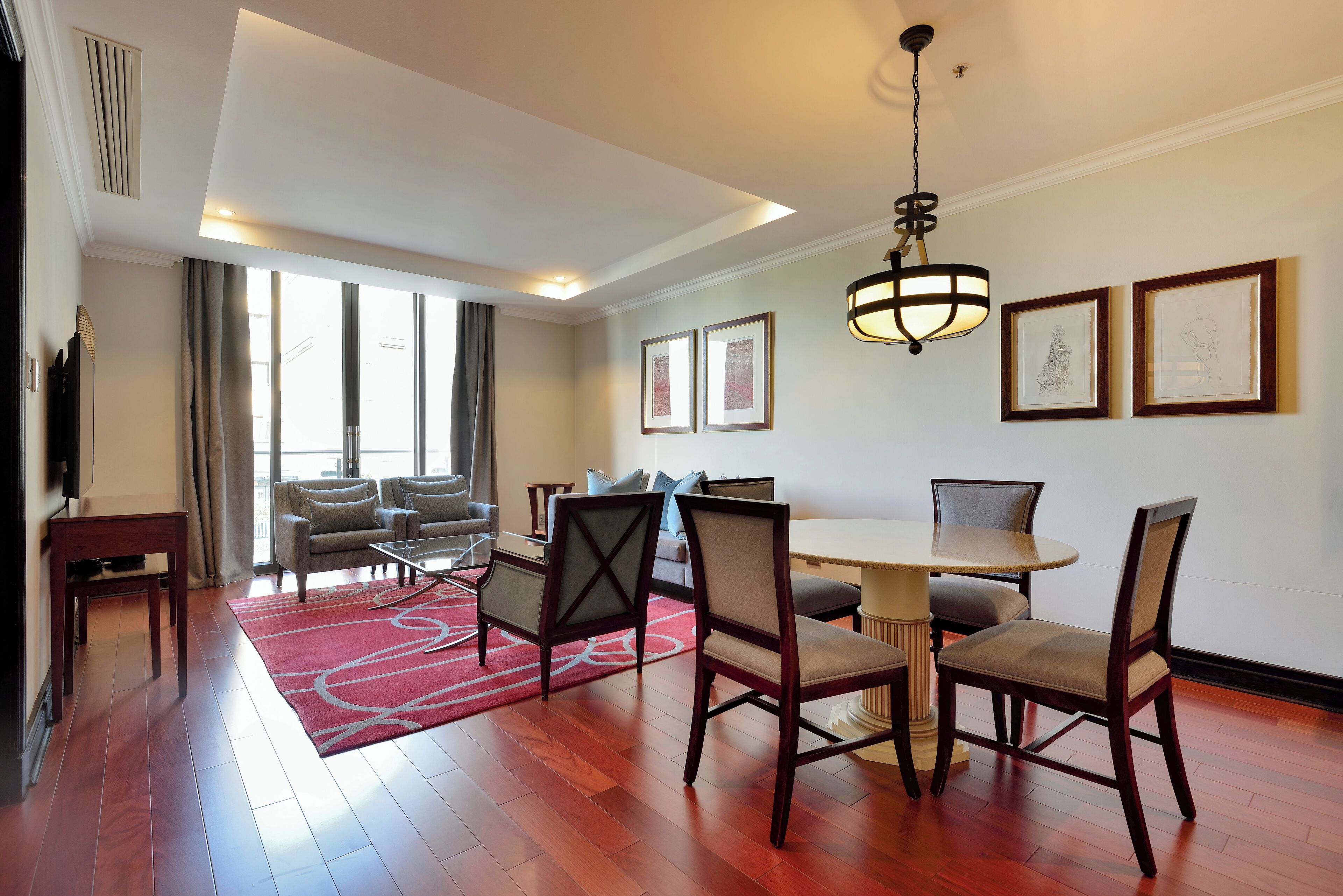 A hotel room with a dining area, a sofa, a TV, and a large window.