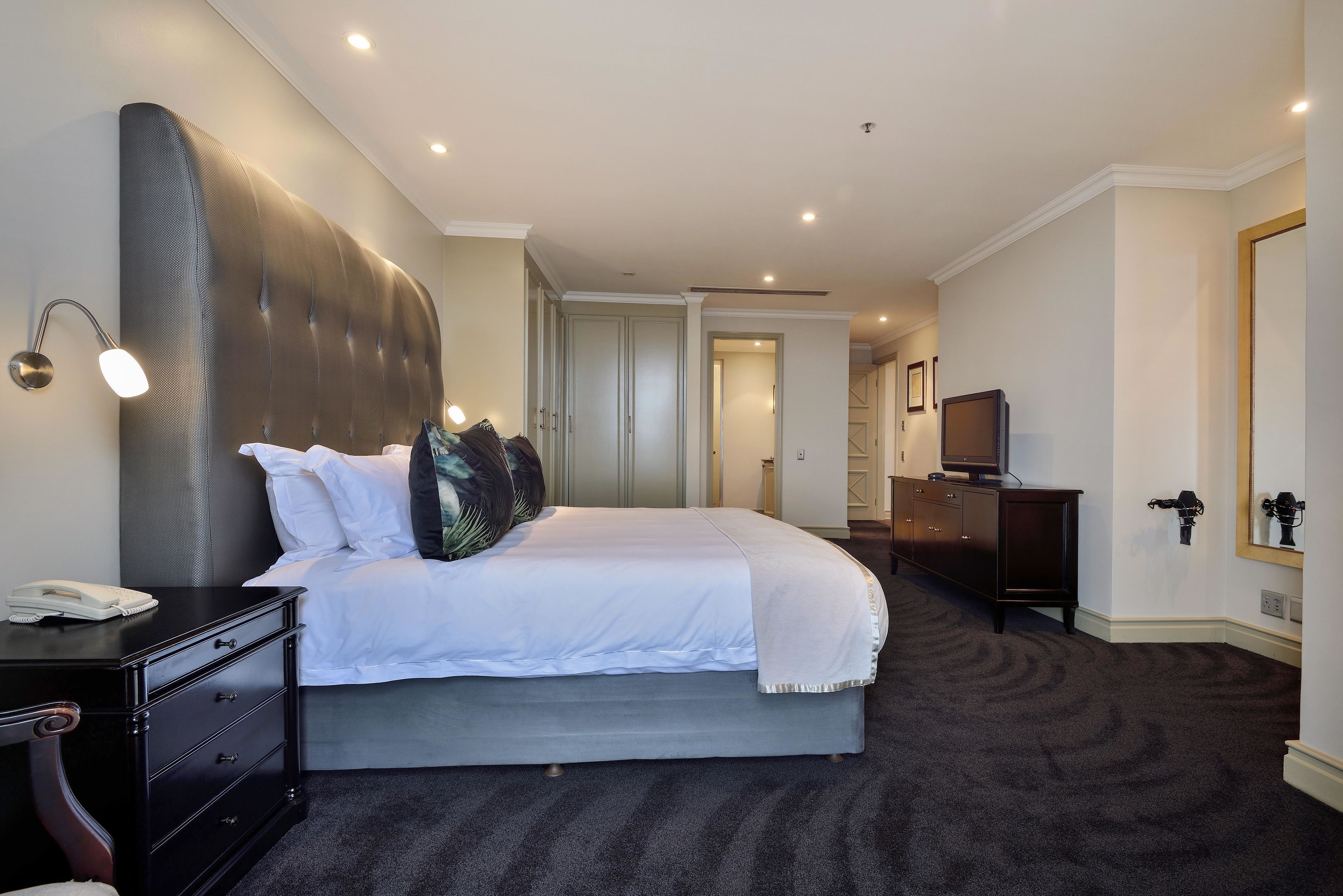 Habitación de hotel ordenada con una cama grande, una mesita de noche con lámpara, un aparador y una televisión.