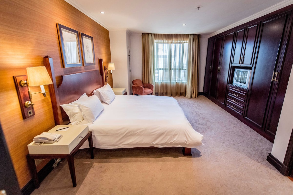 Een hotelkamer met een groot bed, bedlampen, een telefoon, een stoel en een kledingkast.