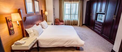 A hotel room with a large bed, bedside lamps, a telephone, a chair, and a wardrobe.