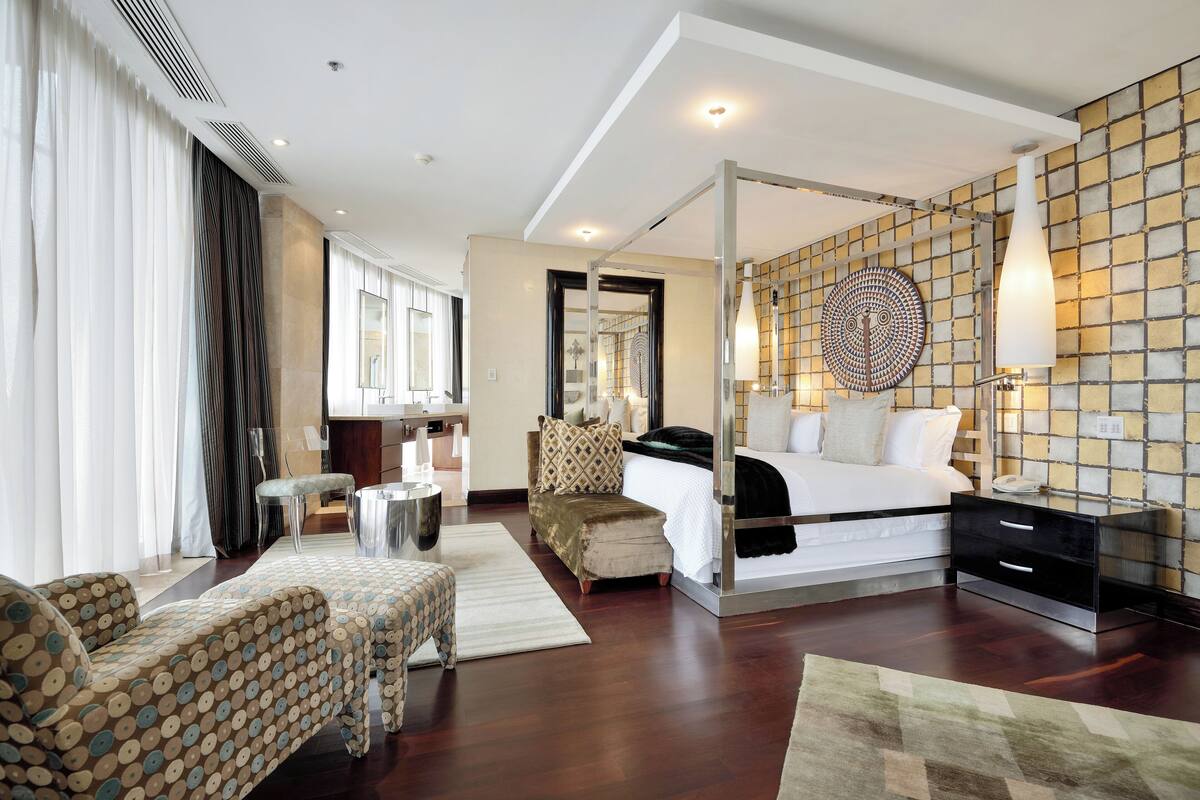 Een moderne hotelkamer met een groot bed, een zithoek met een gestreept sofa, een bijzettafeltje en een decoratief object aan de muur.